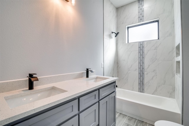 full bathroom featuring double vanity, a textured wall, a sink, and shower / bathing tub combination