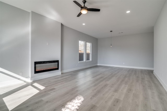 unfurnished living room featuring light wood finished floors, baseboards, a glass covered fireplace, ceiling fan, and recessed lighting