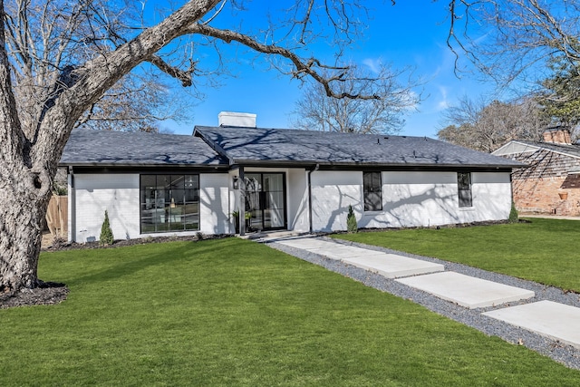 view of front of property with brick siding, a shingled roof, fence, a chimney, and a front yard