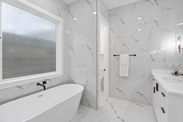 full bath with stone wall, toilet, vanity, marble finish floor, and a soaking tub