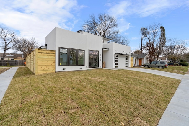 contemporary house with driveway, stucco siding, an attached garage, fence, and a front yard