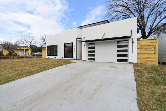 contemporary home featuring a garage, driveway, a front yard, and stucco siding