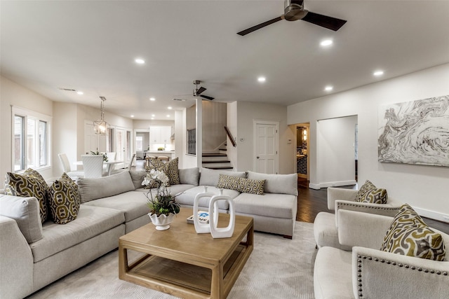 living area featuring light wood-type flooring, stairs, ceiling fan with notable chandelier, and recessed lighting