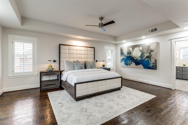 bedroom with dark wood-type flooring, a raised ceiling, visible vents, and baseboards