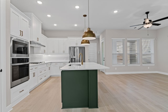 kitchen featuring an island with sink, stainless steel appliances, light countertops, under cabinet range hood, and a sink