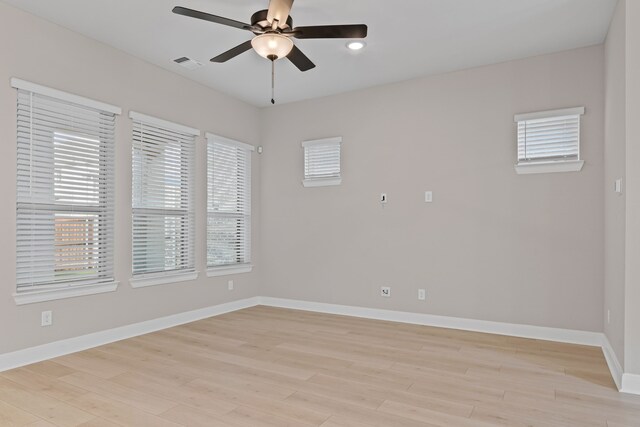 spare room featuring light wood finished floors, a ceiling fan, visible vents, and baseboards