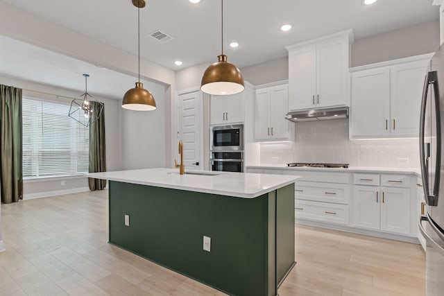 kitchen featuring light wood-style flooring, under cabinet range hood, stainless steel appliances, a sink, and visible vents