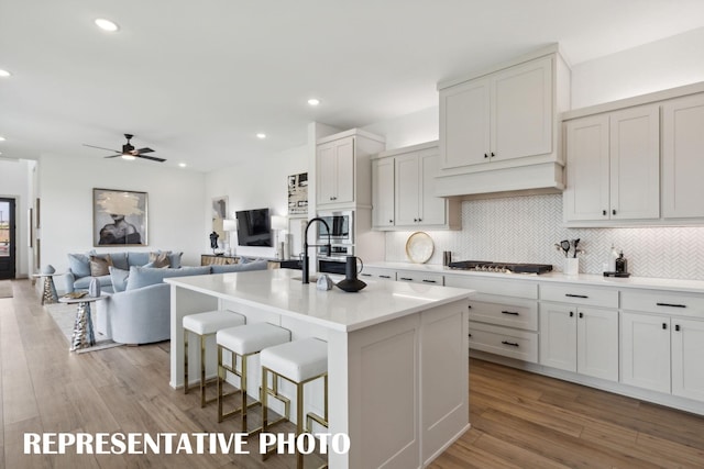 kitchen with white cabinetry, a kitchen breakfast bar, open floor plan, light countertops, and an island with sink