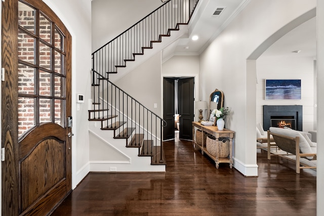 foyer entrance with a lit fireplace, a high ceiling, dark wood finished floors, and visible vents