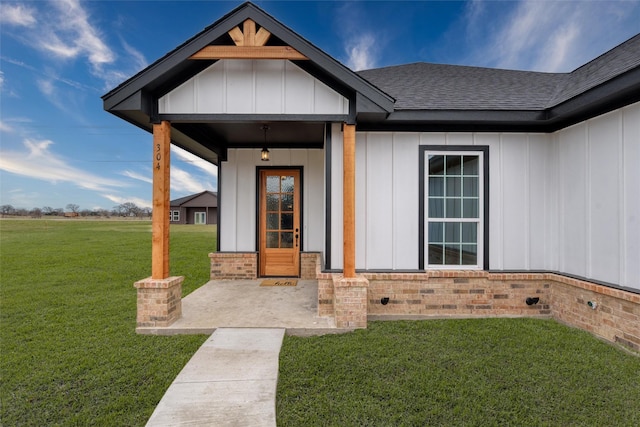 doorway to property featuring a yard, a shingled roof, board and batten siding, and brick siding