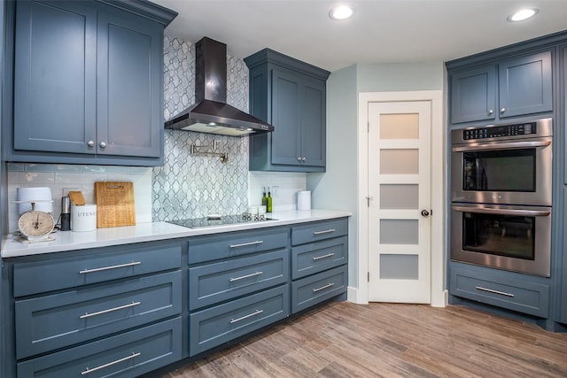 kitchen with stainless steel double oven, dark wood-style flooring, light countertops, wall chimney range hood, and tasteful backsplash