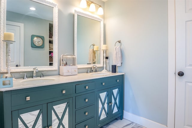 full bath with marble finish floor, double vanity, a sink, and baseboards