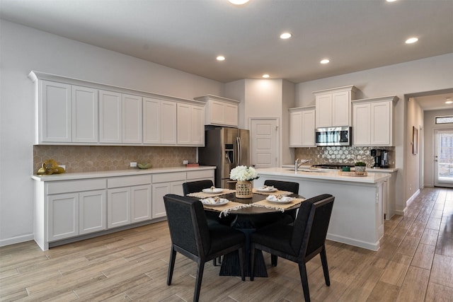 kitchen with stainless steel appliances, a sink, light wood-style floors, light countertops, and an island with sink