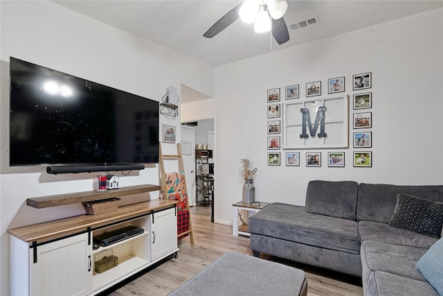 living room featuring a textured ceiling, light wood finished floors, visible vents, and a ceiling fan