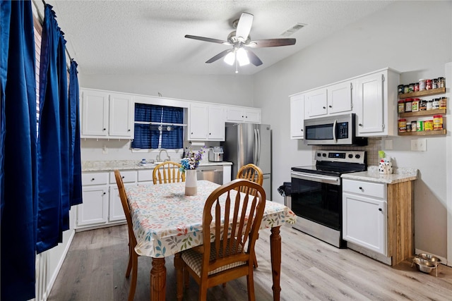 kitchen with vaulted ceiling, light countertops, appliances with stainless steel finishes, and white cabinets