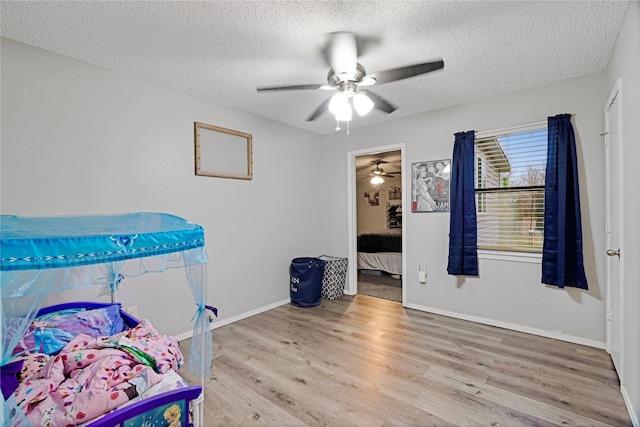 bedroom with baseboards, ceiling fan, light wood-style flooring, and a textured ceiling