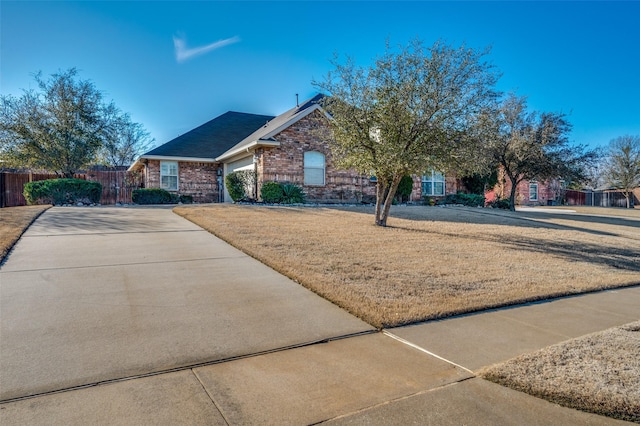 ranch-style home with a front yard, concrete driveway, brick siding, and fence