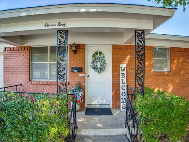 doorway to property featuring covered porch and brick siding