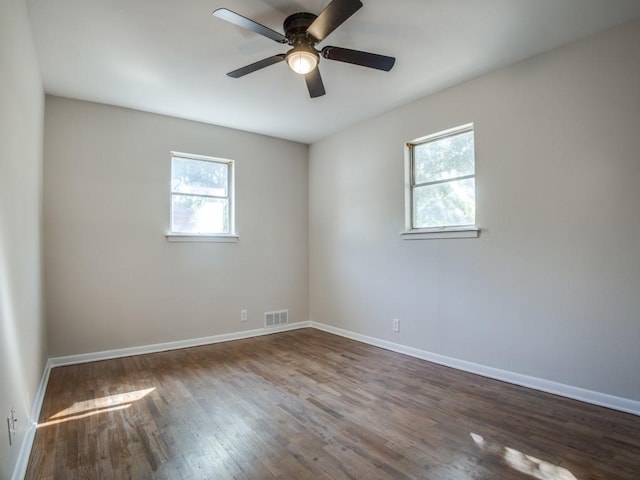 unfurnished room with dark wood-style floors, baseboards, visible vents, and a ceiling fan