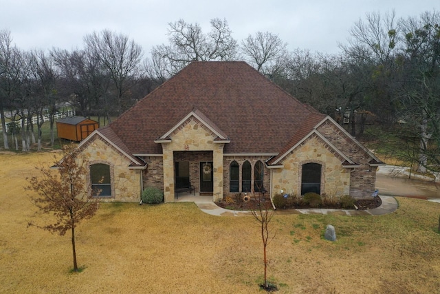 french country style house featuring stone siding, a front lawn, and roof with shingles