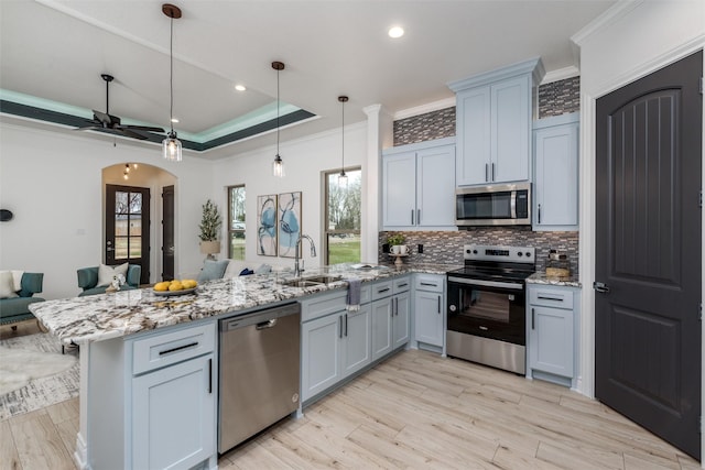 kitchen featuring a sink, appliances with stainless steel finishes, light stone countertops, a raised ceiling, and decorative light fixtures