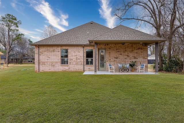 rear view of property with brick siding, roof with shingles, a lawn, and a patio