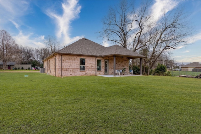 rear view of house featuring brick siding, roof with shingles, a patio, and a yard