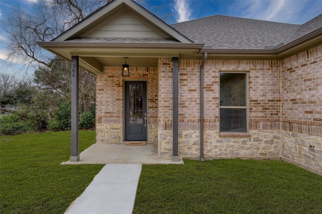 entrance to property featuring a yard, brick siding, roof with shingles, and stone siding