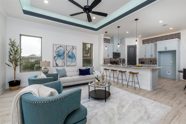 living area featuring light wood-style floors, visible vents, ornamental molding, and a raised ceiling