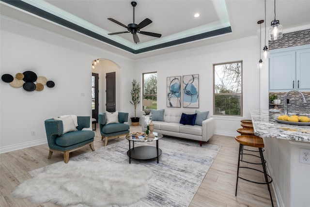 living room featuring a wealth of natural light, arched walkways, crown molding, and a tray ceiling