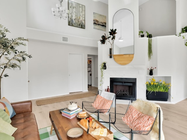 living area featuring a notable chandelier, a high ceiling, a premium fireplace, visible vents, and light wood-style floors