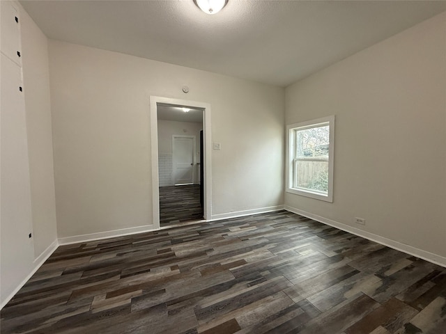 spare room featuring dark wood-style floors and baseboards