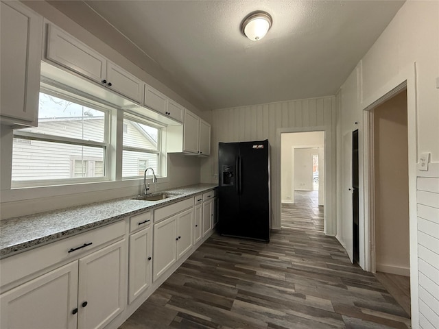 kitchen with light stone counters, white cabinets, black refrigerator with ice dispenser, and a sink