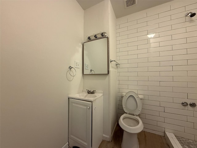 full bath with toilet, wood finished floors, vanity, visible vents, and a tile shower