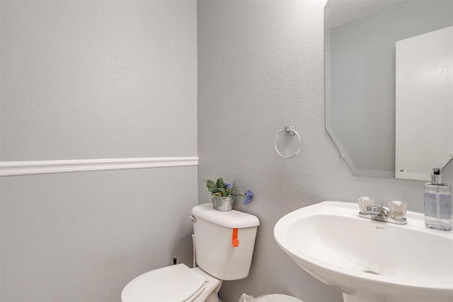 bathroom with toilet, a textured wall, and a sink