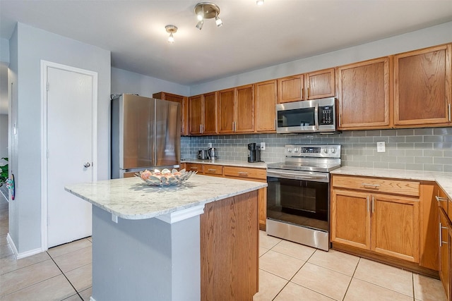 kitchen featuring light stone counters, a kitchen island, tasteful backsplash, stainless steel appliances, and light tile patterned flooring