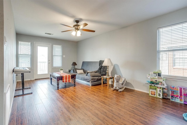 sitting room with a wealth of natural light, visible vents, ceiling fan, and wood finished floors