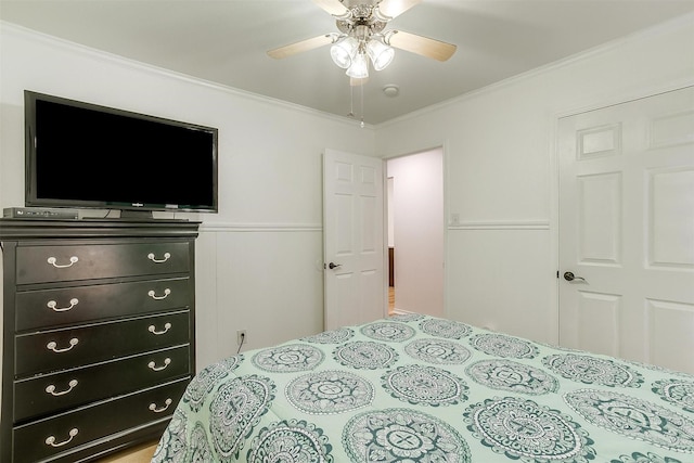 bedroom with ceiling fan, crown molding, and wainscoting