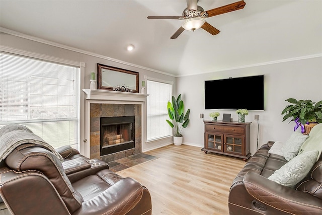 living room with a fireplace, lofted ceiling, light wood-style flooring, ornamental molding, and a ceiling fan