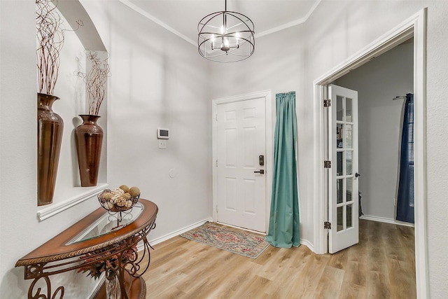 foyer with baseboards, ornamental molding, a chandelier, and wood finished floors