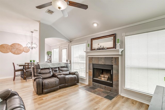 living room with lofted ceiling, visible vents, light wood-style floors, ornamental molding, and a tile fireplace