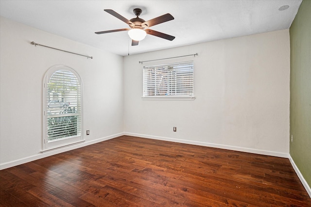 empty room featuring dark wood-type flooring, a ceiling fan, and baseboards