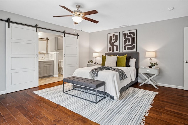 bedroom with a barn door, baseboards, dark wood-type flooring, and ensuite bathroom