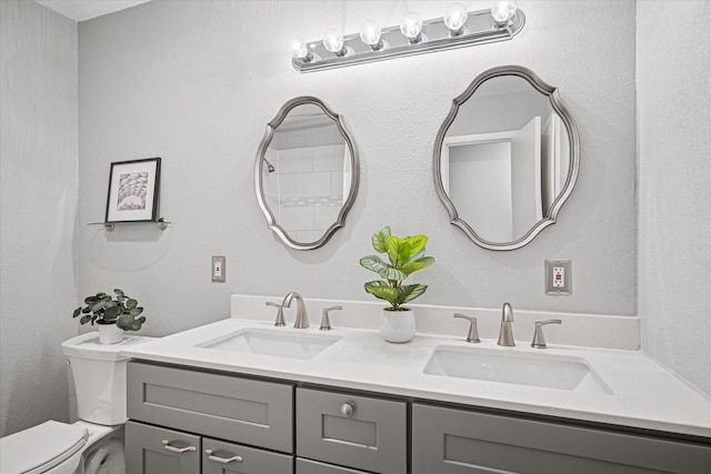 full bath with toilet, double vanity, and a sink