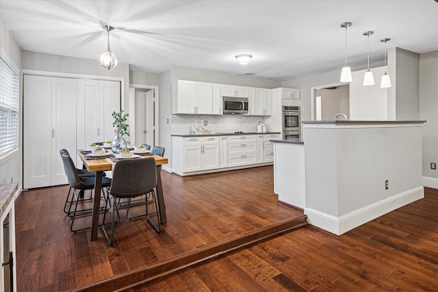 kitchen featuring hanging light fixtures, dark countertops, white cabinets, and stainless steel appliances