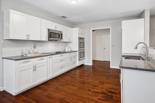 kitchen featuring visible vents, white cabinets, dark countertops, stainless steel appliances, and a sink