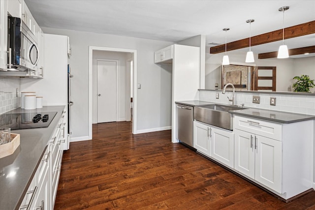 kitchen featuring white cabinets, dark countertops, decorative light fixtures, stainless steel appliances, and a sink