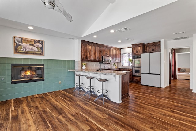 kitchen featuring a breakfast bar, dark wood-style flooring, stainless steel appliances, visible vents, and a peninsula