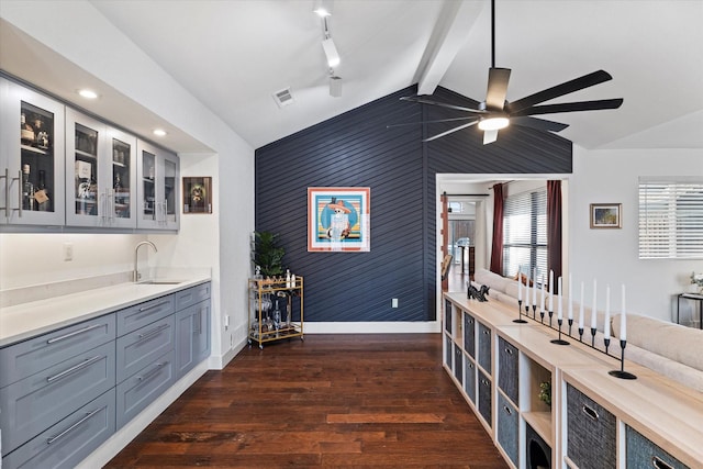 kitchen featuring glass insert cabinets, vaulted ceiling with beams, a sink, and dark wood-style floors