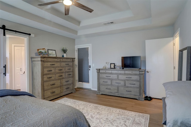 bedroom with a tray ceiling, a barn door, light wood-style floors, and visible vents